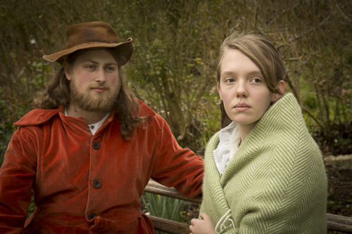 Man in casual russet jacket and soft hat siting on bench with girl wrapped in green shawl