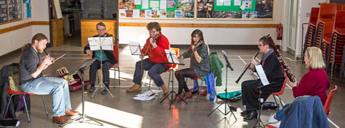 Group of six people sitting in a hall playing instruments