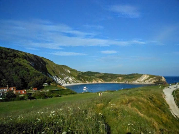 View of Lulwoth Cove, with blue sea, blue sky and green grass in the foreground
